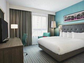 Modern hotel room with a large bed, tufted headboard, teal accent wall, and sleek furniture
