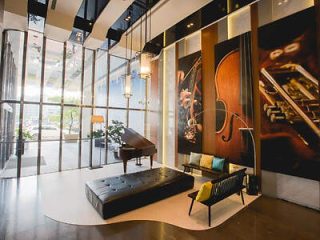 Modern lobby featuring a grand piano, seating area with a black bench and chairs, and large musical instrument murals on the wall. Floor-to-ceiling windows let in natural light from outside.