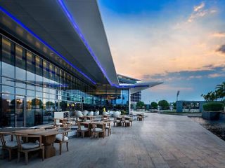 Outdoor restaurant patio with wooden tables and chic seating, modern architecture, and blue accent lighting under a twilight sky.