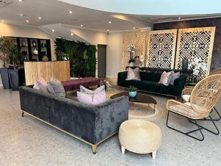 A stylish hotel lobby furnished with a velvet sofa, rattan chair, and ornate mirrors, exuding a chic and modern atmosphere.