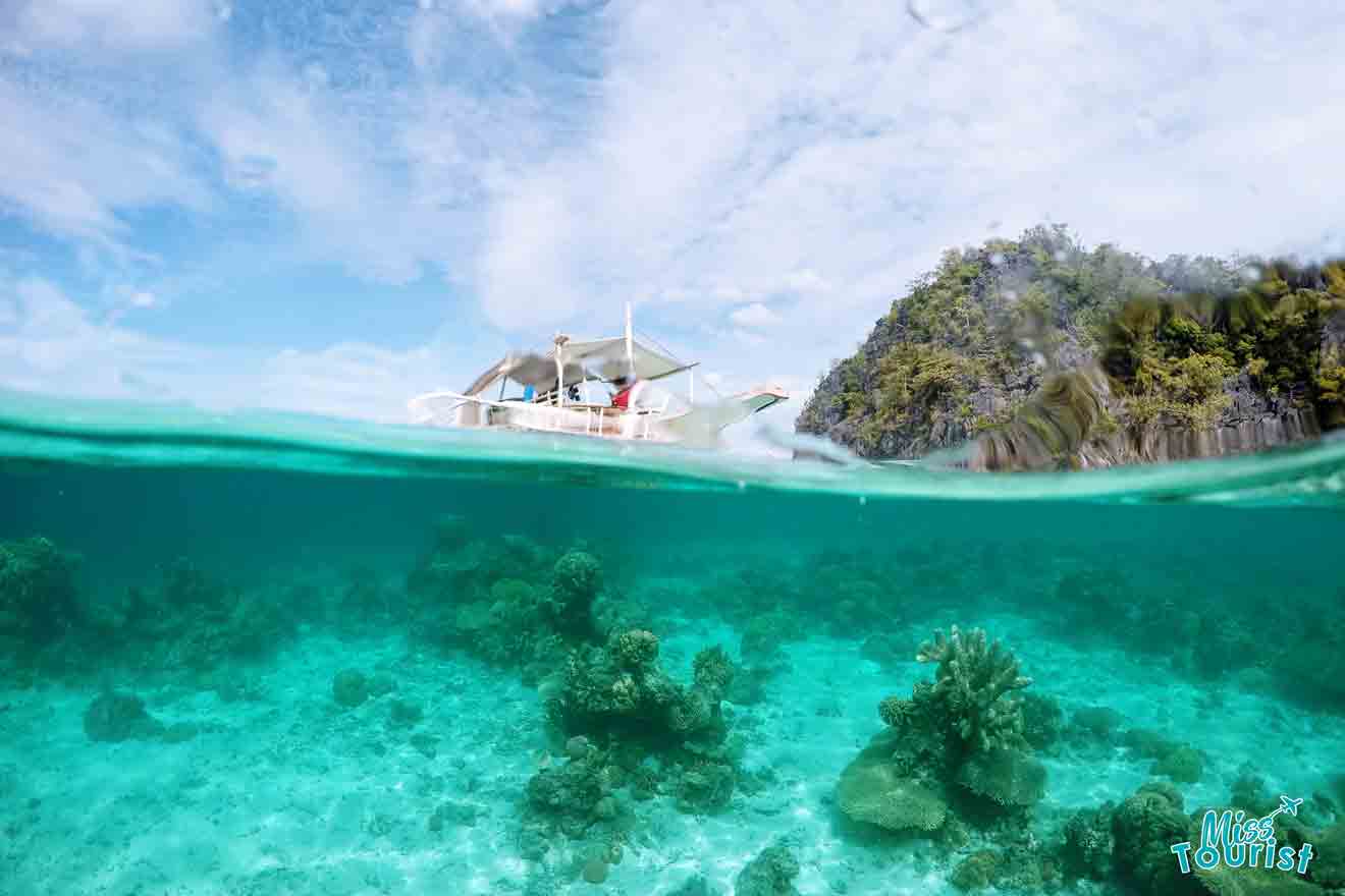 A boat floats on a clear, turquoise sea near a rocky island. The underwater view shows coral formations.