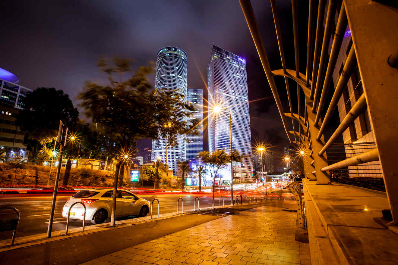 Night scene of a bustling city street with modern skyscrapers illuminated against the night sky in Tel Aviv.
