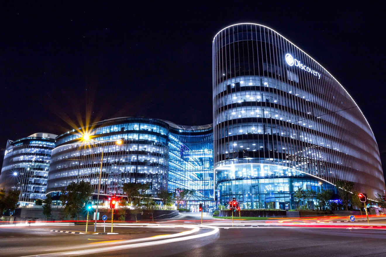 Night view of the curved, illuminated Discovery headquarters building in Sandton, Johannesburg, with light streaks from passing traffic