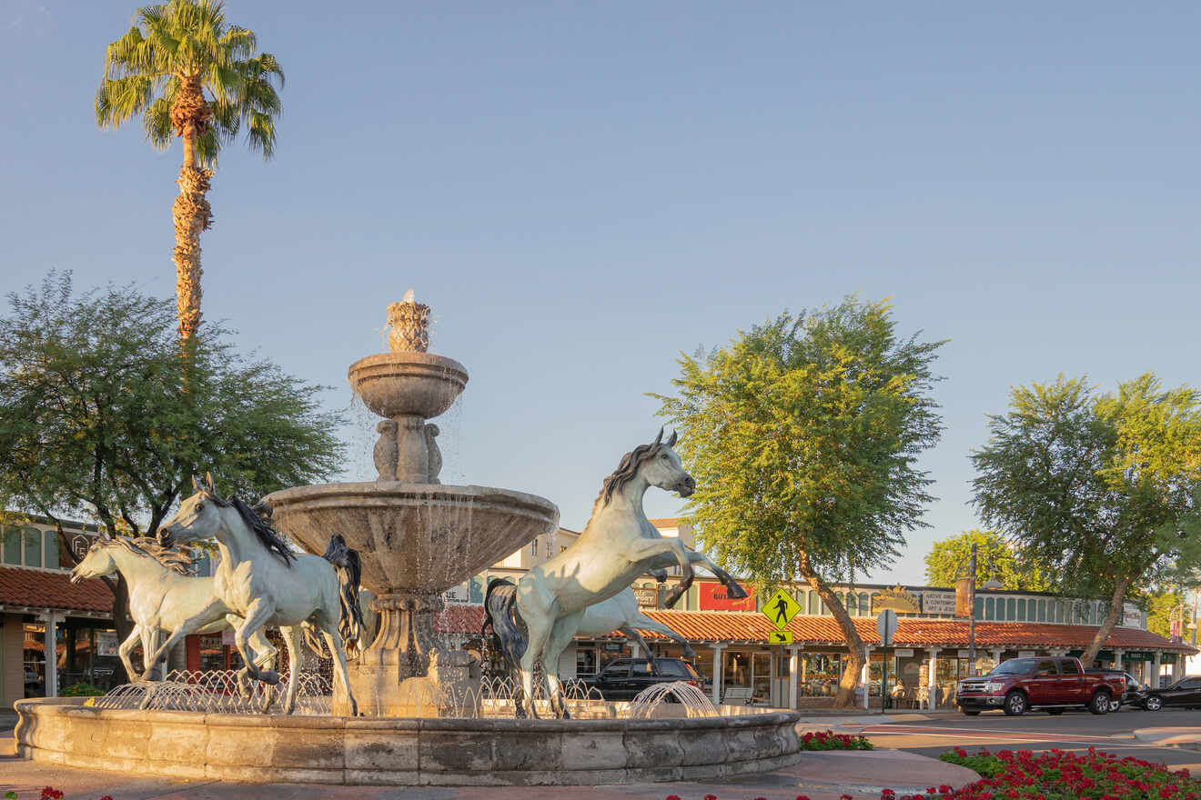 A fountain with horse sculptures surrounded by palm trees and buildings in a sunny plaza in Scottsdale