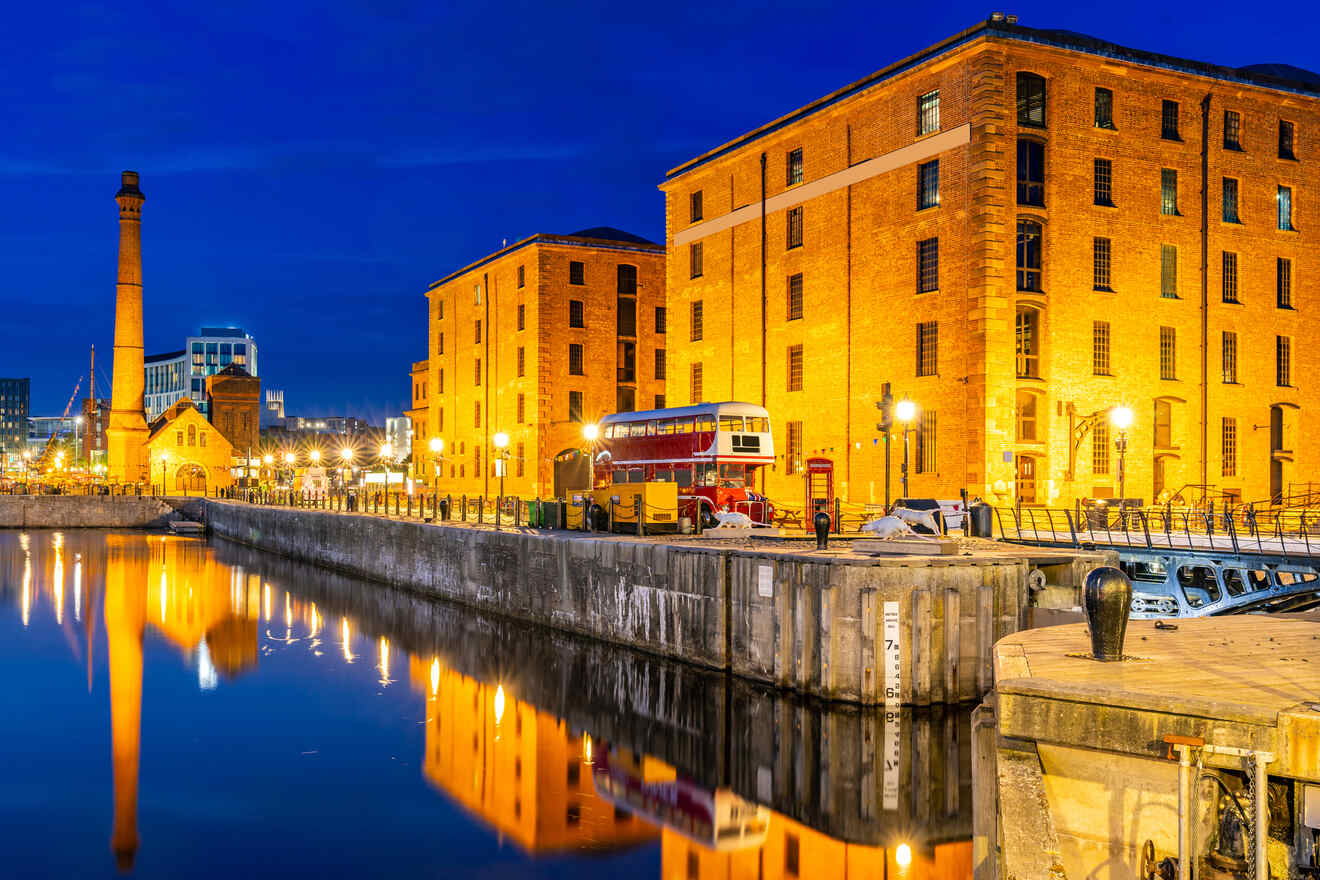 Liverpool's Albert Dock at twilight, with historic warehouses reflected in the water, a vintage bus on display, and a vibrant blue hour sky.