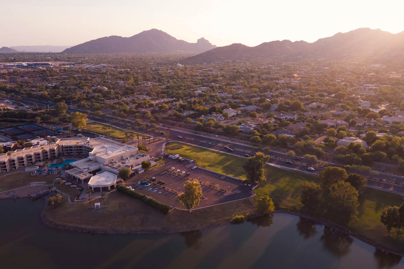 An aerial view of Scottsdale with mountains, a large building complex, and roads, taken at sunset.
