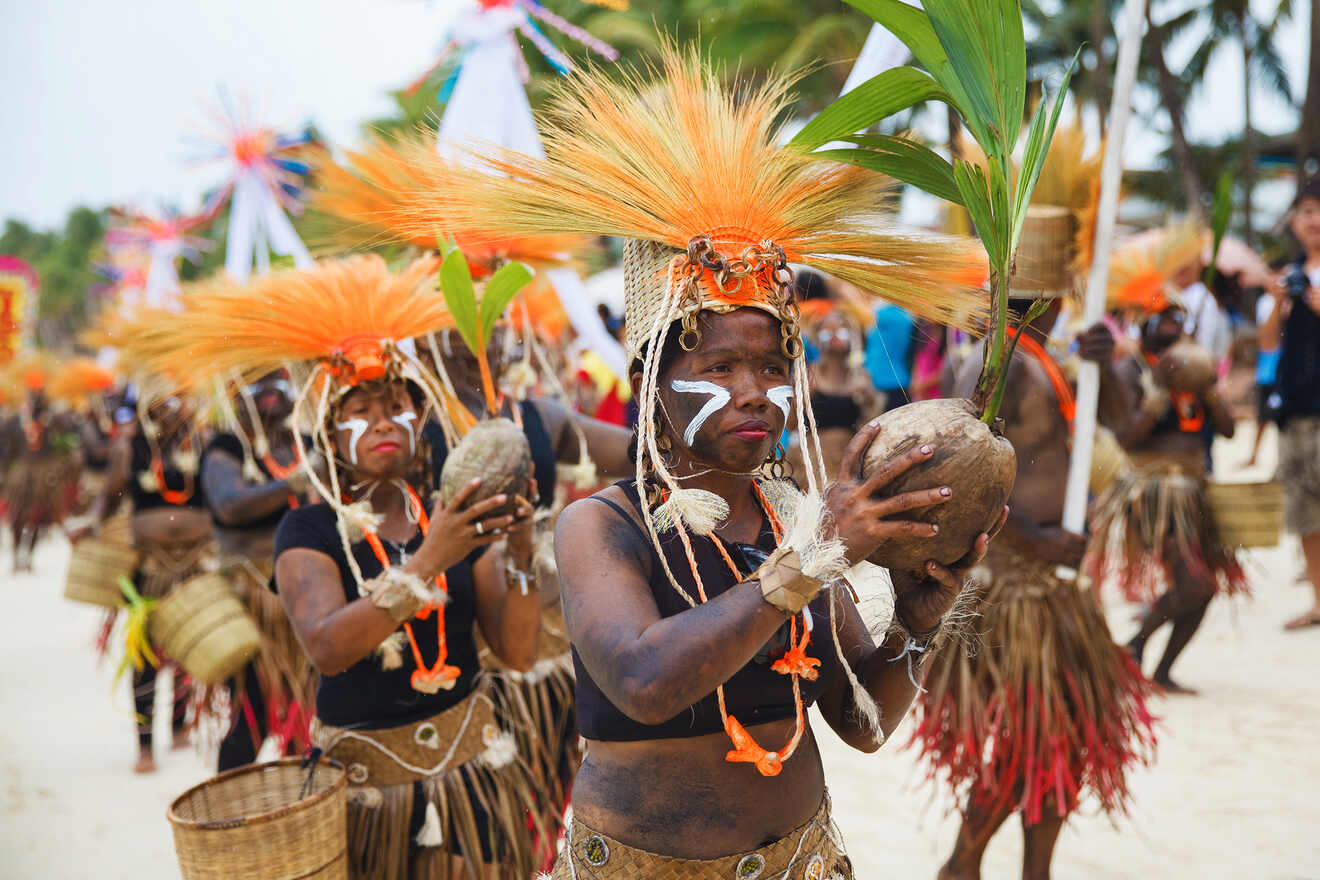 A vibrant traditional dance performance by indigenous people in elaborate tribal costumes, including feathered headdresses, during a cultural festival on a beach.