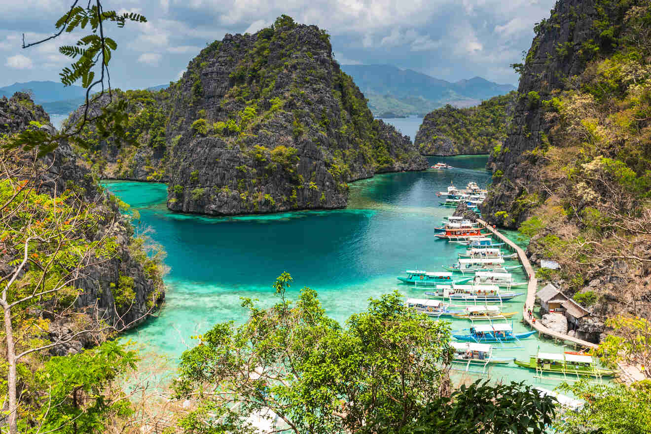 A stunning view of a secluded lagoon surrounded by steep cliffs and lush vegetation, with boats moored along a narrow beach.