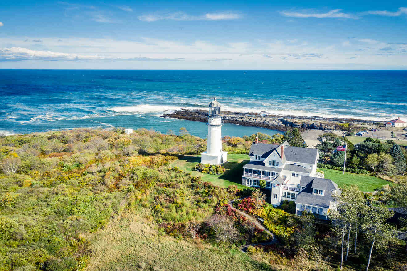 Aerial view of a picturesque lighthouse on a coastal headland with a classic New England home and vibrant fall foliage.
