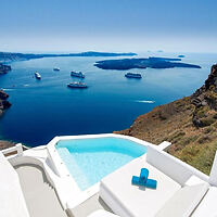 Infinity pool with a stunning view of the caldera in Santorini, Greece, featuring clear blue skies and anchored ships.