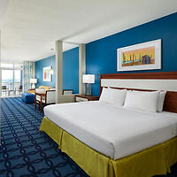 Bright hotel room with two queen beds, blue accent wall, and abstract artwork above the headboards
