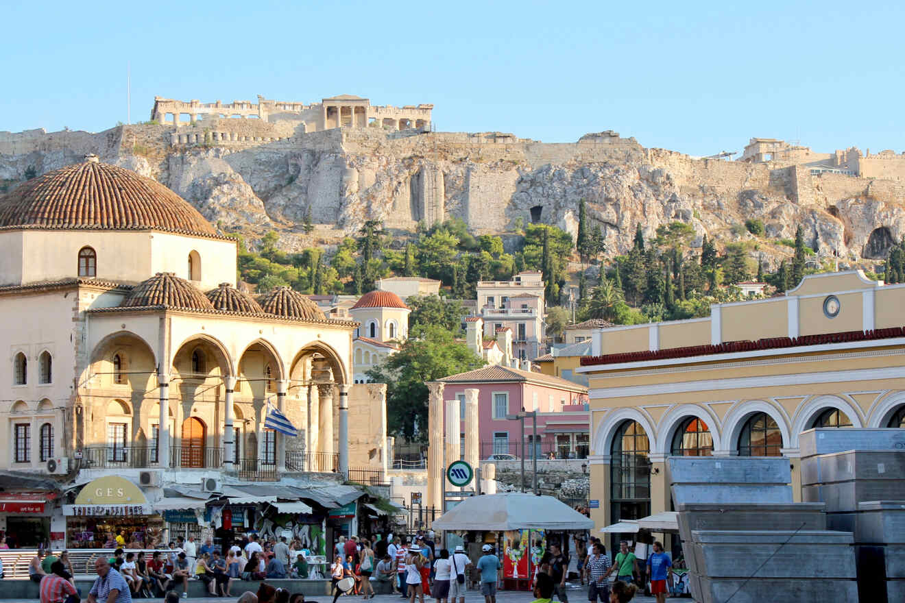 Bustling square in Athens with a view of the Acropolis in the distance and Monastiraki Mosque in the foreground.
