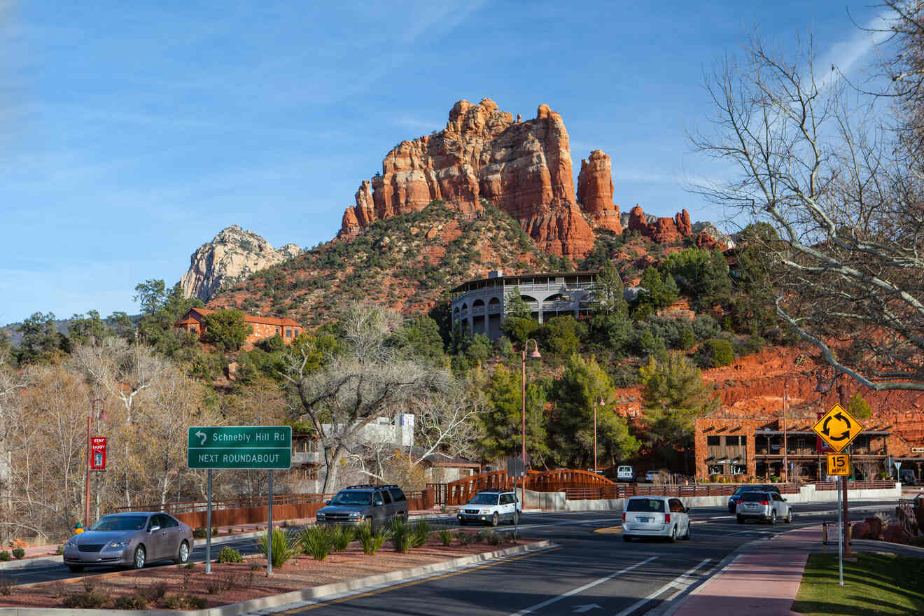 A bustling street scene in Sedona with red rock formations in the background and a prominent sign for Schnebly Hill Road