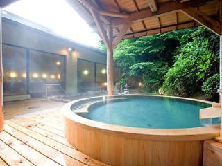 A serene outdoor onsen bath surrounded by wood decking and lush foliage