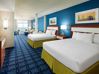 Double queen room in a hotel with blue carpet, lime green bed runners, and a framed painting on the wall