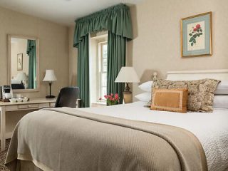 Classic hotel bedroom with a beige comforter, floral wall art, and a small desk with a view of the window
