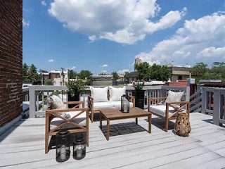Cozy rooftop terrace with wooden furniture and plush pillows, overlooking an urban landscape