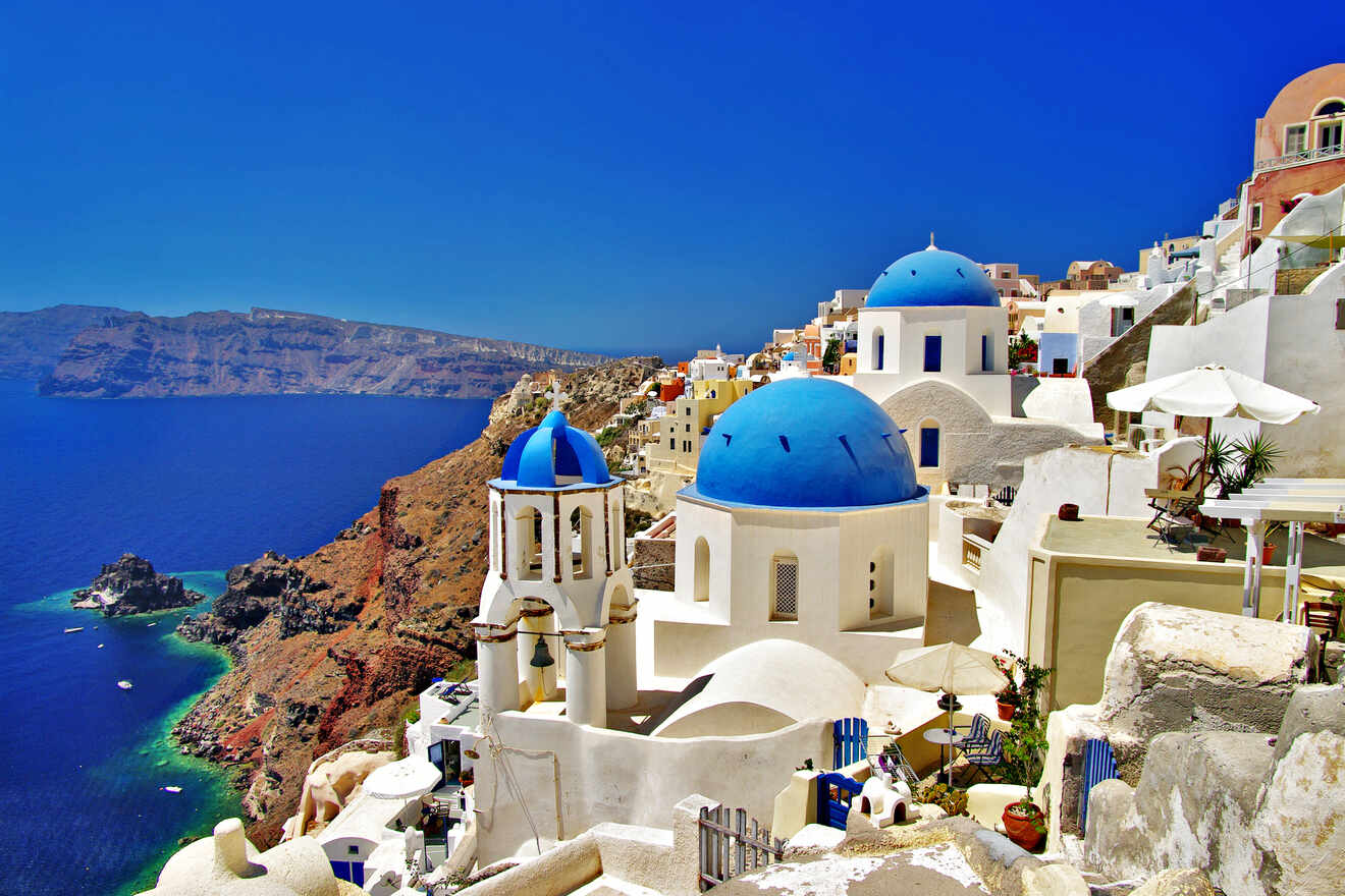Iconic white buildings with blue domes in Oia, Santorini, overlooking the Aegean Sea under a bright blue sky.
