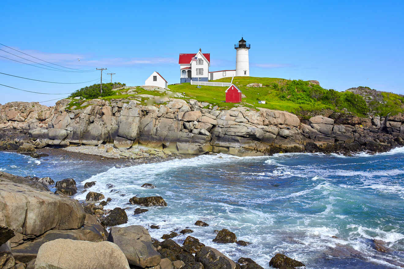 Historic lighthouse and keeper's house on a rocky shoreline against a clear blue sky.
