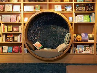 A modern reading nook with a round, cushioned seat embedded in a bookshelf wall filled with various books