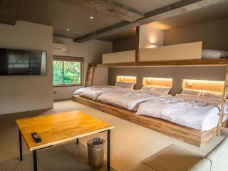 A spacious hotel room with contemporary bunk beds, a seating area, and a large window revealing greenery outside