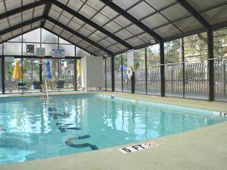 Enclosed indoor swimming pool with a retractable roof, lifebuoy, and deck chairs visible in a serene setting
