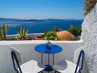 Quaint balcony with blue chairs overlooking the Aegean Sea in Santorini, capturing the essence of Greek island tranquility.