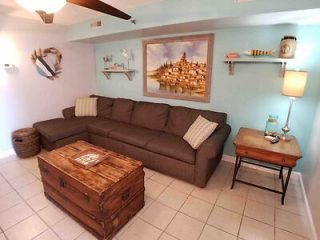 Coastal-themed living room with a brown sofa, nautical wall art, and a wooden chest coffee table