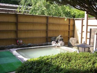Private outdoor onsen bath in a traditional Japanese garden setting with a bamboo fence and stone decorations