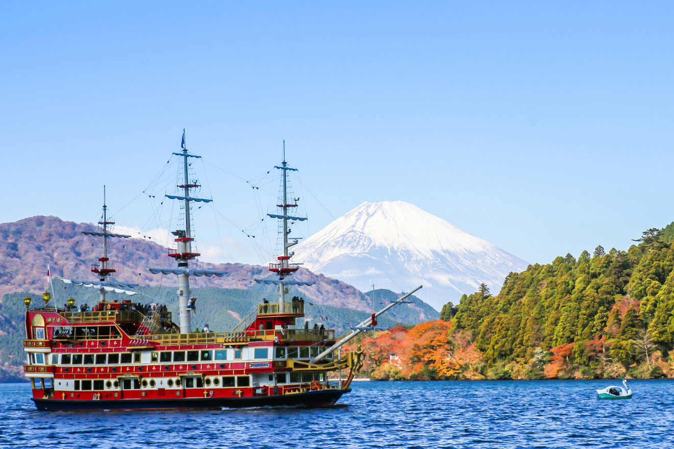 A pirate ship cruise on a blue lake with Mount Fuji in the backdrop amidst a clear sky and colorful autumn trees on the shore