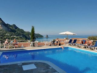 Hotel pool with a view of the Ionian Sea, surrounded by loungers and parasols, with guests enjoying the sun.