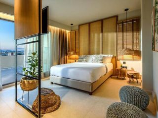 Elegant hotel room with a neutral color scheme, large bed, floor-to-ceiling windows, and modern furnishings.