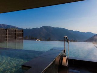 Infinity onsen bath with a stunning view of mountains under a clear blue sky, visible from the edge of the water
