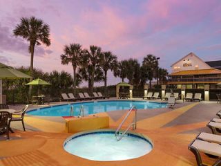 Twilight view of a hotel pool with palm trees, against a backdrop of a sunset sky with hues of pink and blue