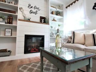 Cozy living room with modern decor and a fireplace, styled with a 'Be Our Guest' sign and comfortable seating.