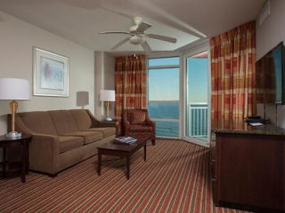 Hotel suite with a brown sofa, patterned curtains, and a balcony overlooking the expansive ocean