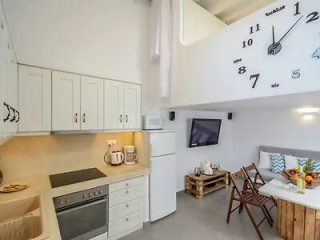 Neat and functional kitchenette with white cabinets, large wall clock, and a small dining area.