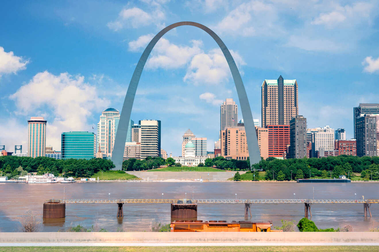 A picturesque cityscape featuring a prominent arch monument, surrounded by a skyline of diverse buildings and the river in the foreground