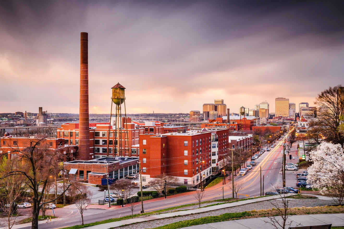 Richmond, Virginia's cityscape at dusk with historic brick buildings, a towering chimney, and a water tower against a colorful sky.