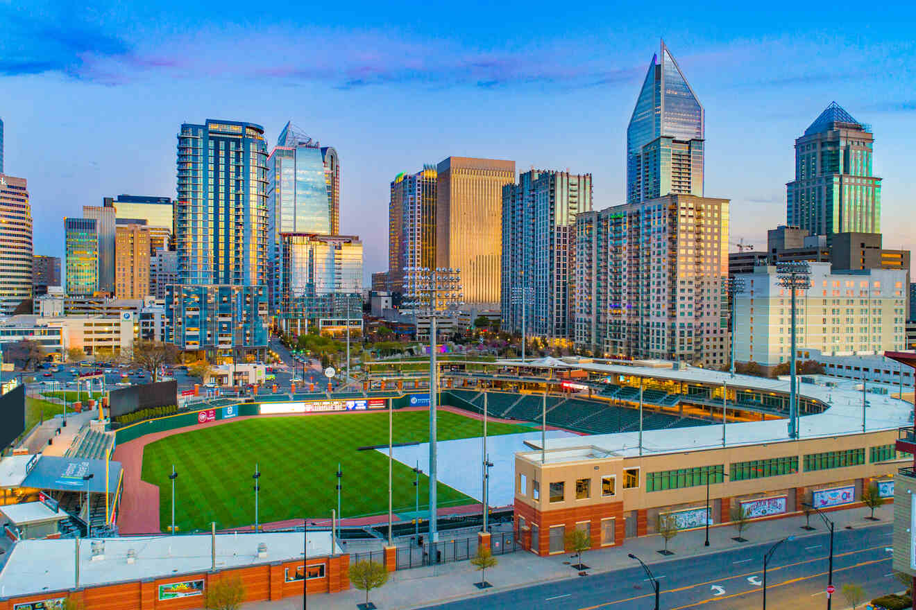 Aerial view of Charlotte's cityscape at dusk, with the baseball stadium in the foreground and skyscrapers lit up