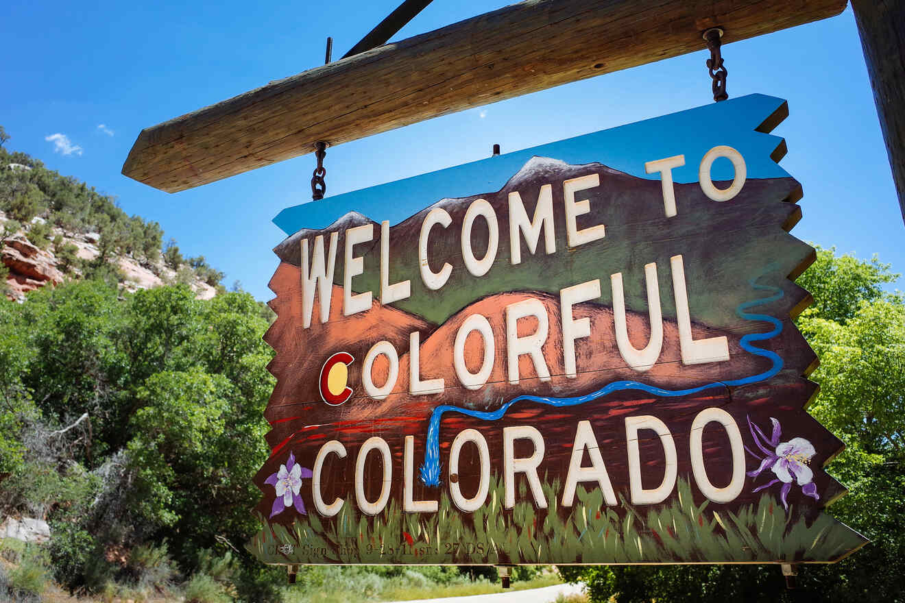 A wooden sign reading "Welcome to Colorful Colorado" is set against a backdrop of trees and a rocky landscape.