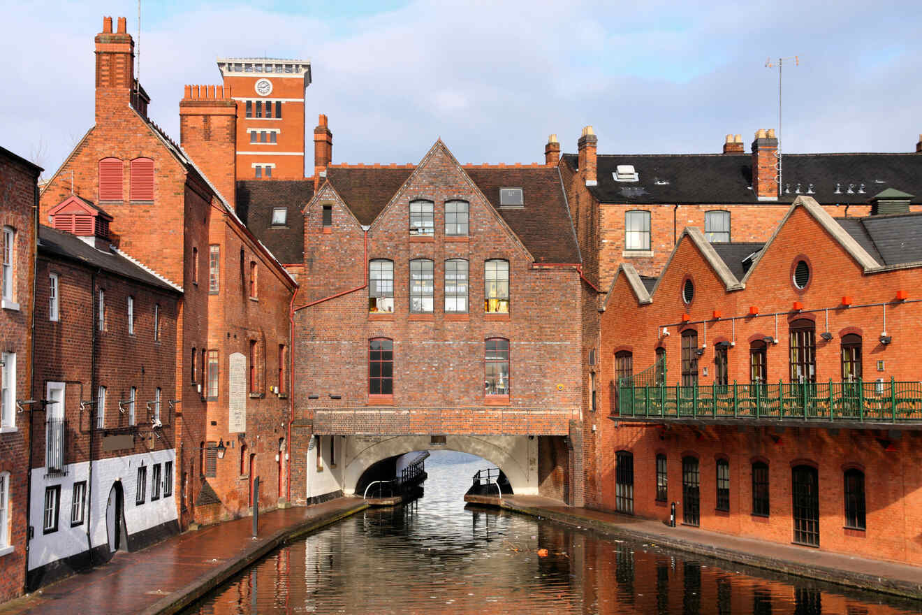 Historic red brick buildings with arched bridge over a calm canal in an urban setting, reflecting on the water's surface
