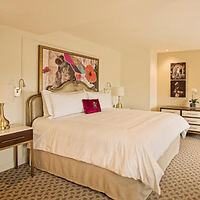 A luxurious hotel room with a large bed, contemporary artwork above the headboard, and tasteful decor