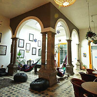 Spacious hostel interior with white arches, hanging hammocks, a variety of seating options, and eclectic decorations on tiled floors