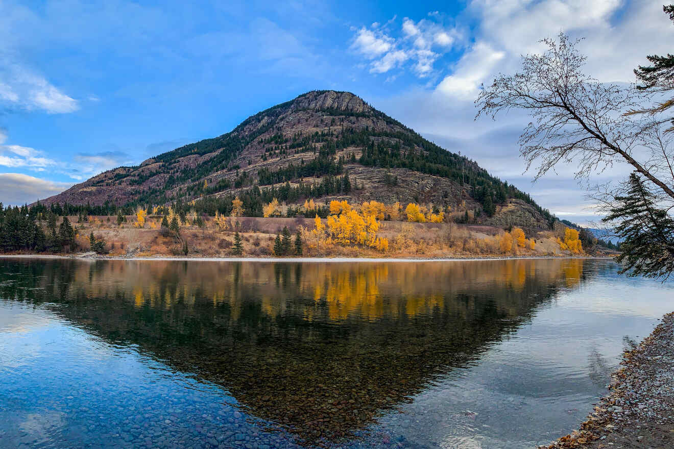 A tranquil autumn scene by a calm lake reflecting a hill covered in yellow and green foliage under a partly cloudy sky