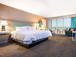 A spacious hotel room with a king-sized bed, floor-to-ceiling windows, and an ocean view