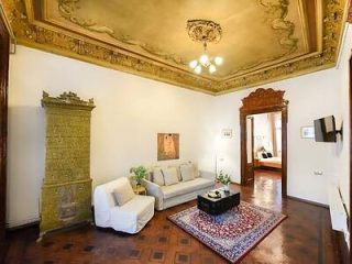 A spacious living room with ornate ceiling details, a decorative fireplace, elegant furnishings, and a classical European charm