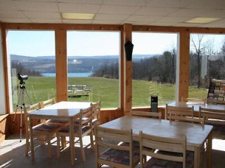 A spacious dining area with large windows offering an expansive view of a serene lake and rolling countryside