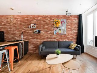 Modern apartment living space with a brick accent wall, comfortable grey couch, and vibrant wall art