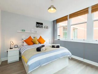 Modern minimalist bedroom with a comfortable double bed, accented with vibrant orange pillows, under soft ambient lighting